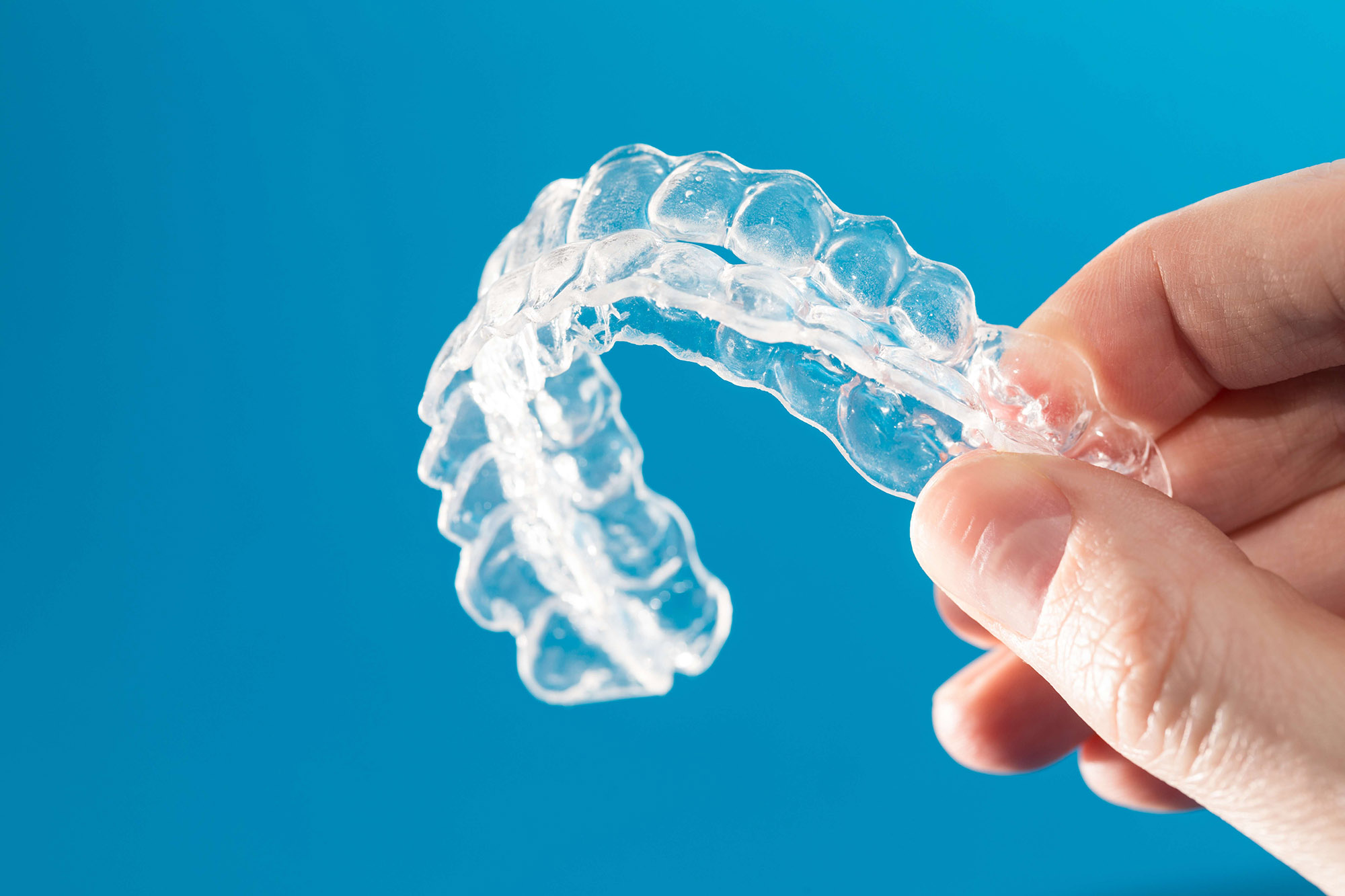 Clear retainers being held against a blue background.